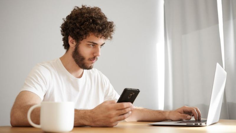 Мужчина сидит за столом с ноутбуком и телефоном и создает домовой чат